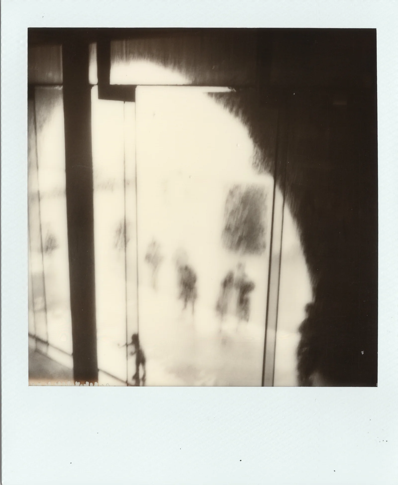 Pale monochrome Polaroid artwork with shadowy vertical forms.