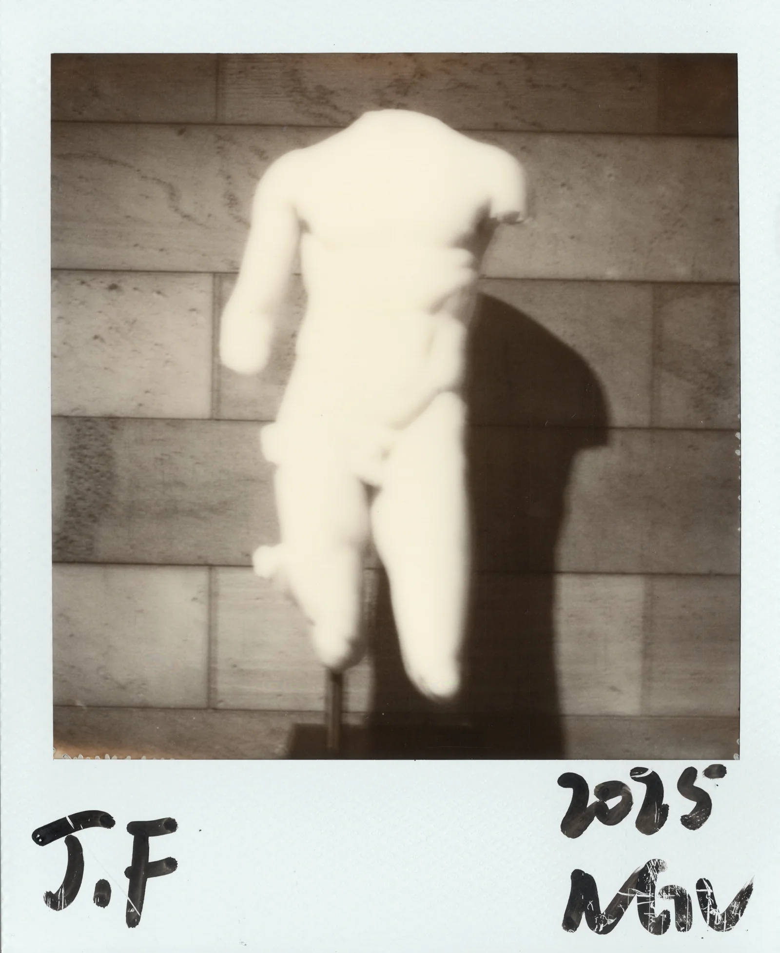 Polaroid artwork of a pale classical body fragment against stone.
